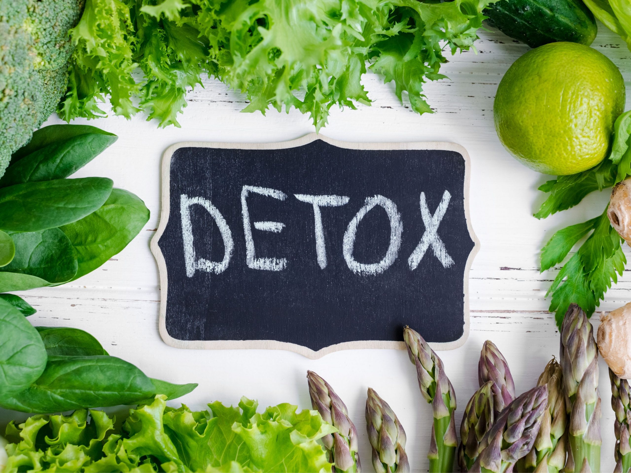A chalkboard with the word “Detox” written on it, surrounded by fresh greenery and herbs.