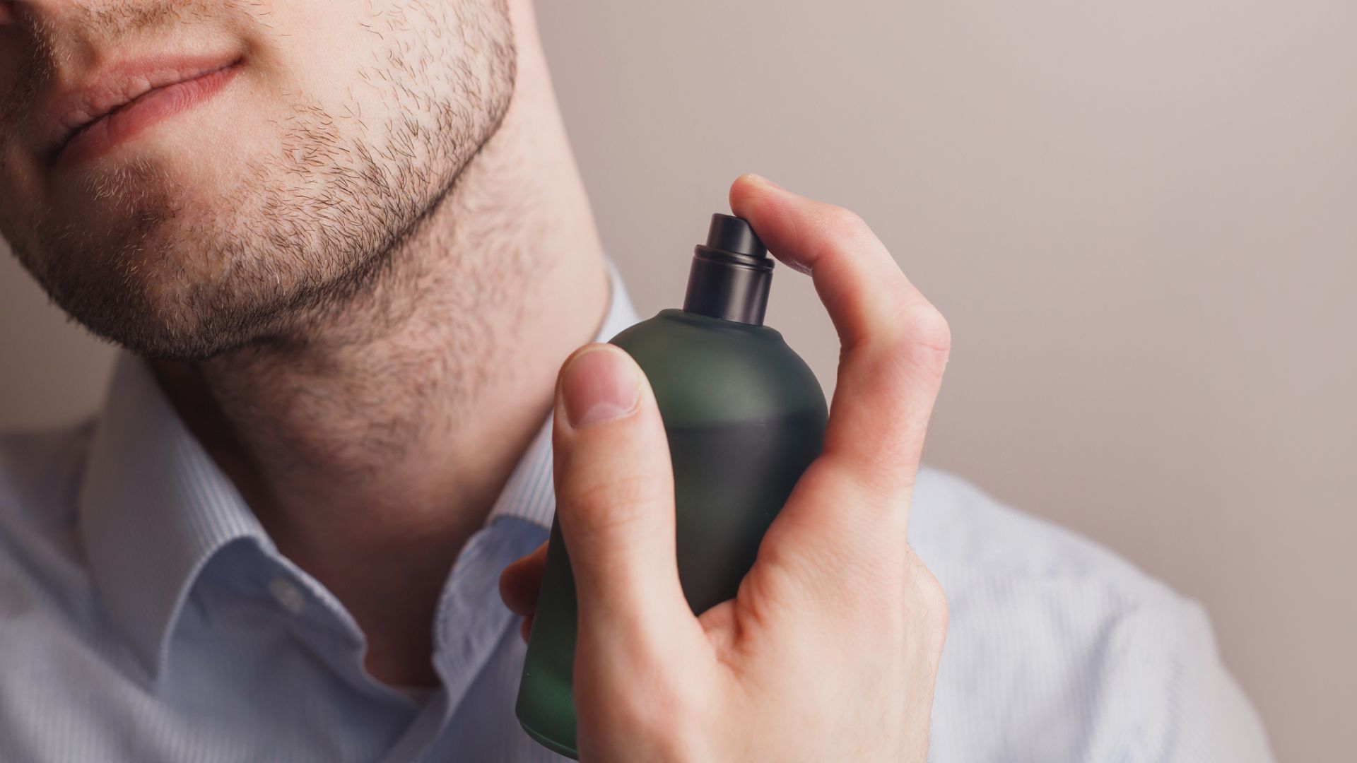 A man in a dress shirt applying cologne to his neck, highlighting proper fragrance application on pulse points.