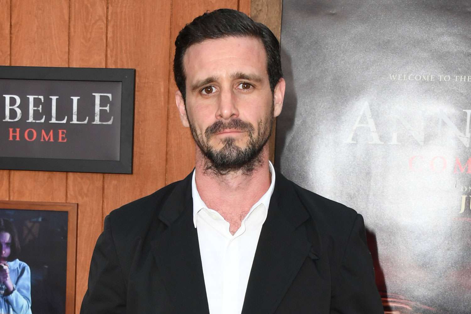 James Ransone looking serious and composed while posing on the red carpet, dressed in a tailored suit with bright lights and photographers in the background.