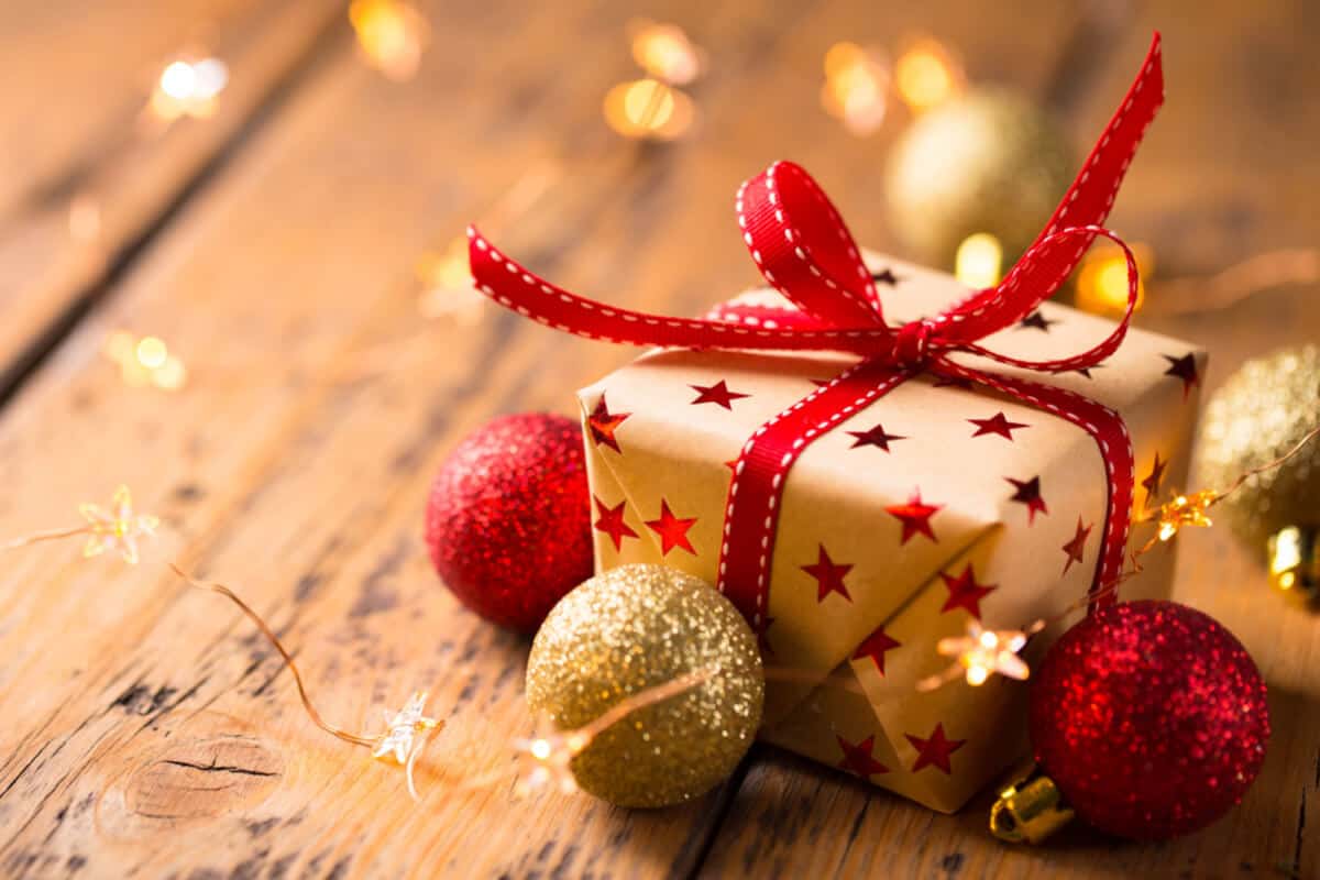 A neatly wrapped Christmas present placed next to colorful festive baubles on a holiday-themed surface.