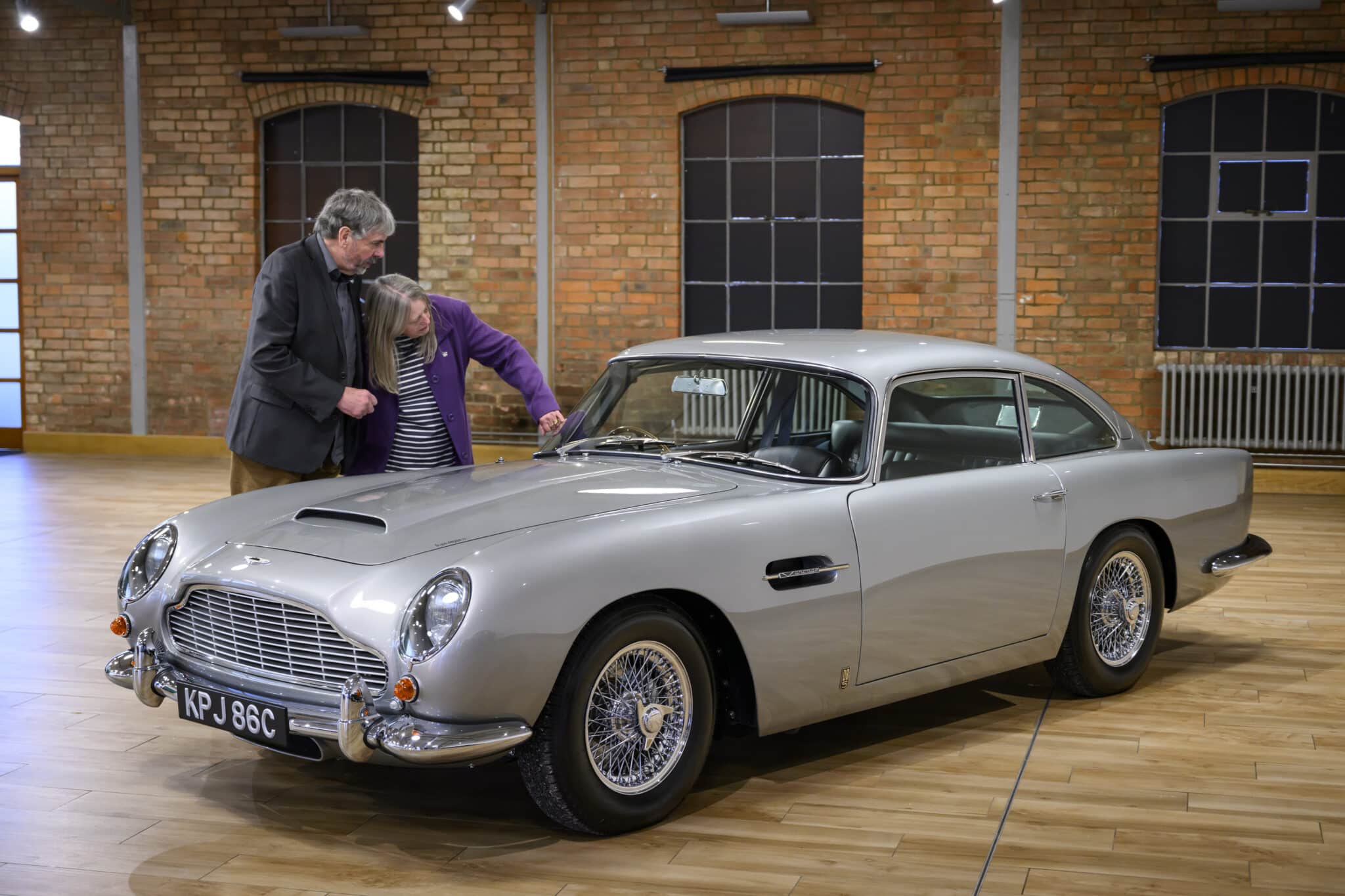 Mr. and Mrs. Williams standing beside their fully refurbished classic car at home, admiring the restored details and polished finish.