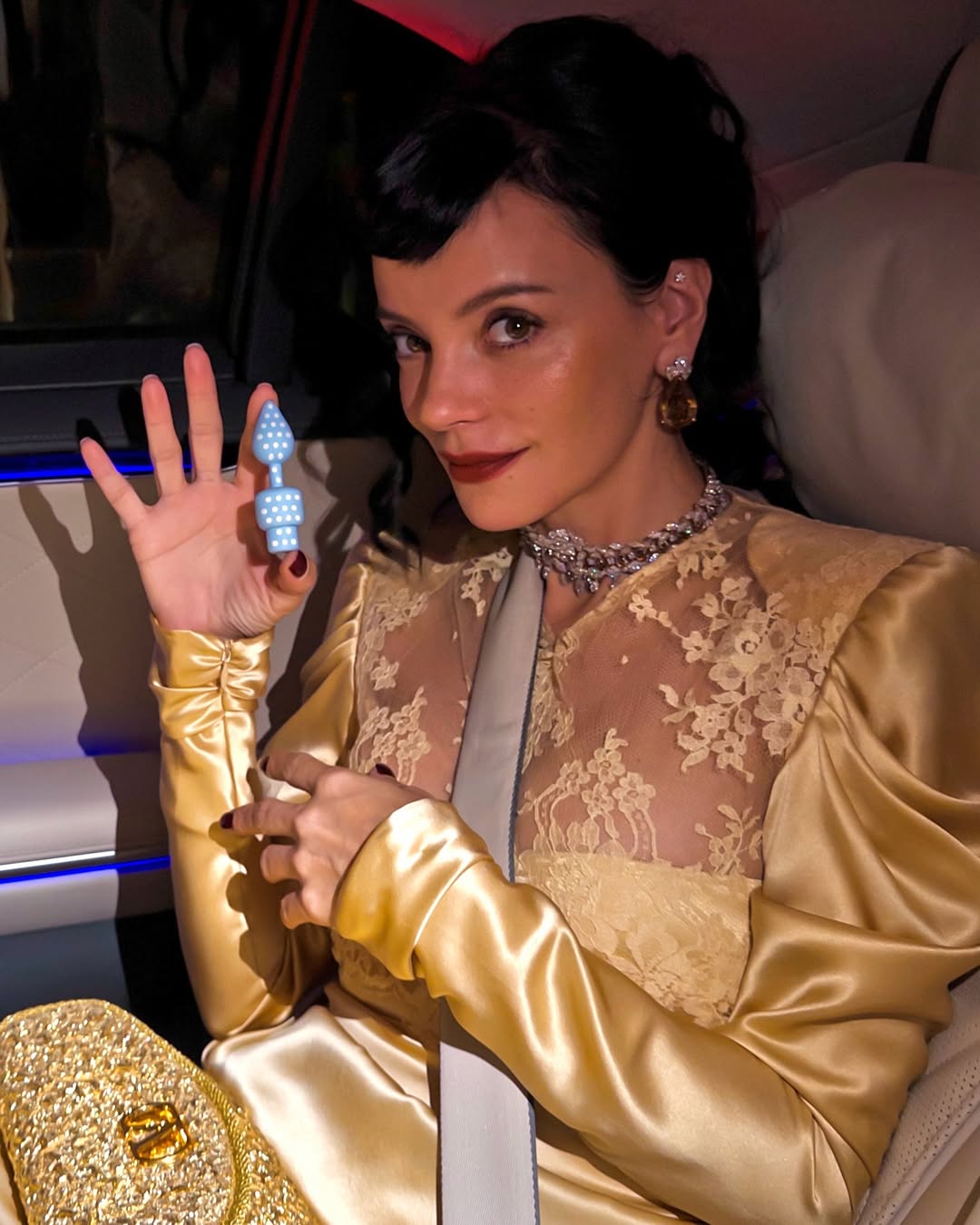 Lily Allen holding a blue-and-white polka-dotted USB shaped like a butt plug during a promotional photoshoot for her West End Girl album.