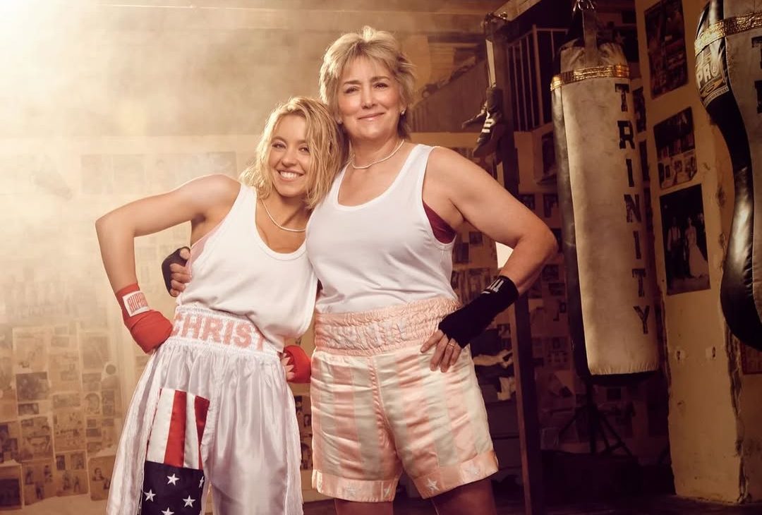 Sydney Sweeney and Christy Martin share a warm, emotional hug during their Sports Illustrated photoshoot, both smiling softly under studio lights, capturing the bond formed through telling Christy’s story.