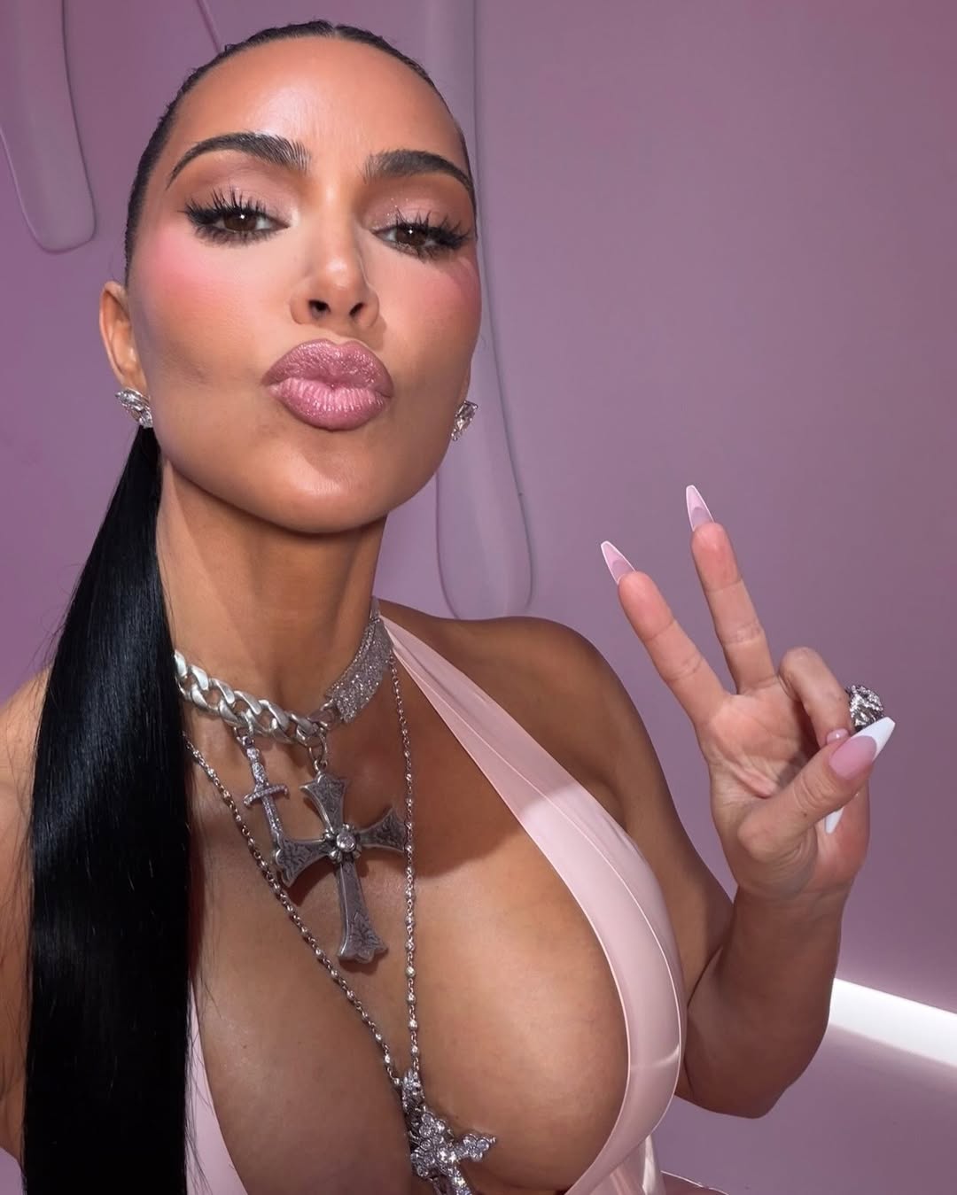 Kim Kardashian flashing a peace sign while wearing a low-cut top, smiling for a playful selfie.