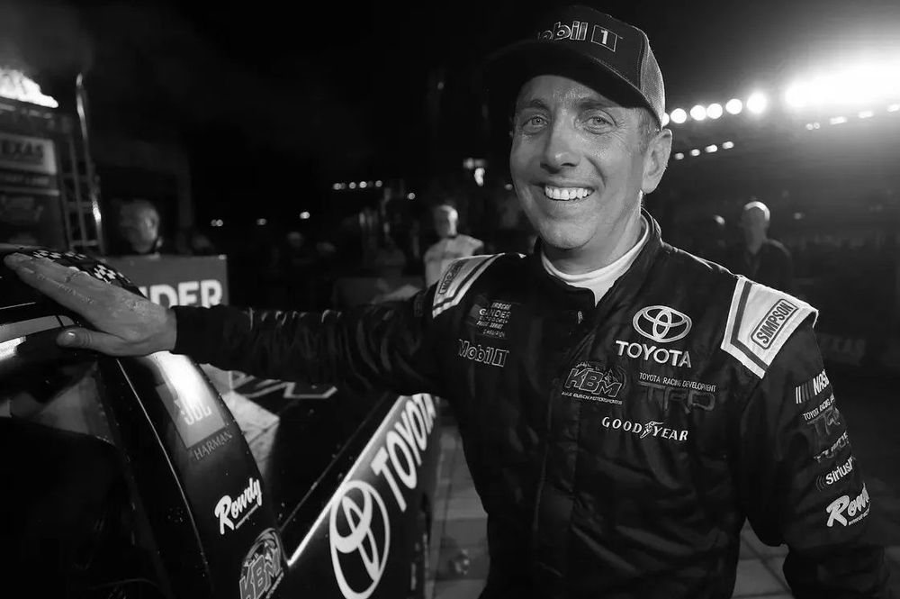 Black and white image of NASCAR driver Greg Biffle touching the roof of his race car in a quiet pre-race moment before heading onto the track.