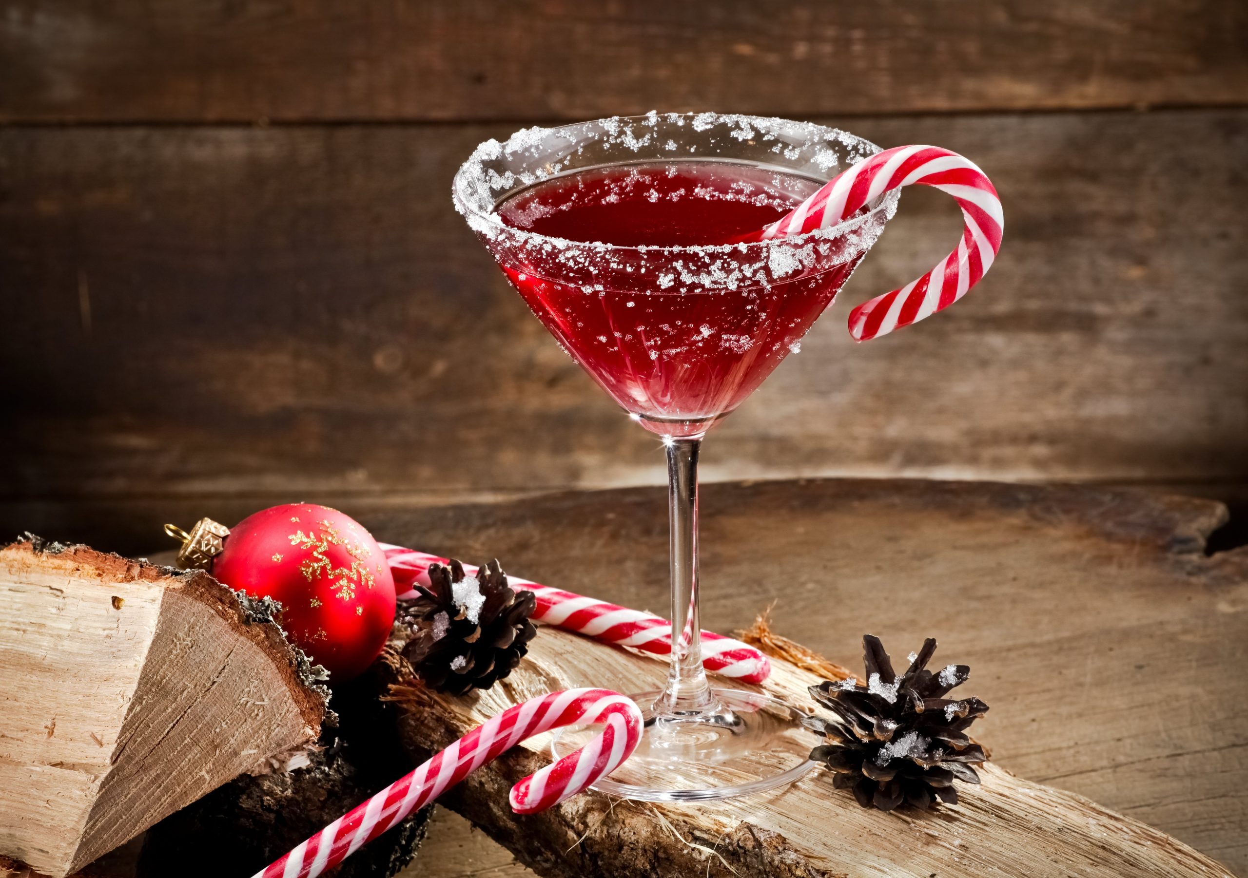 A festive Christmas cocktail in a glass, garnished with a cinnamon stick and cranberry sprig, surrounded by holiday decorations.