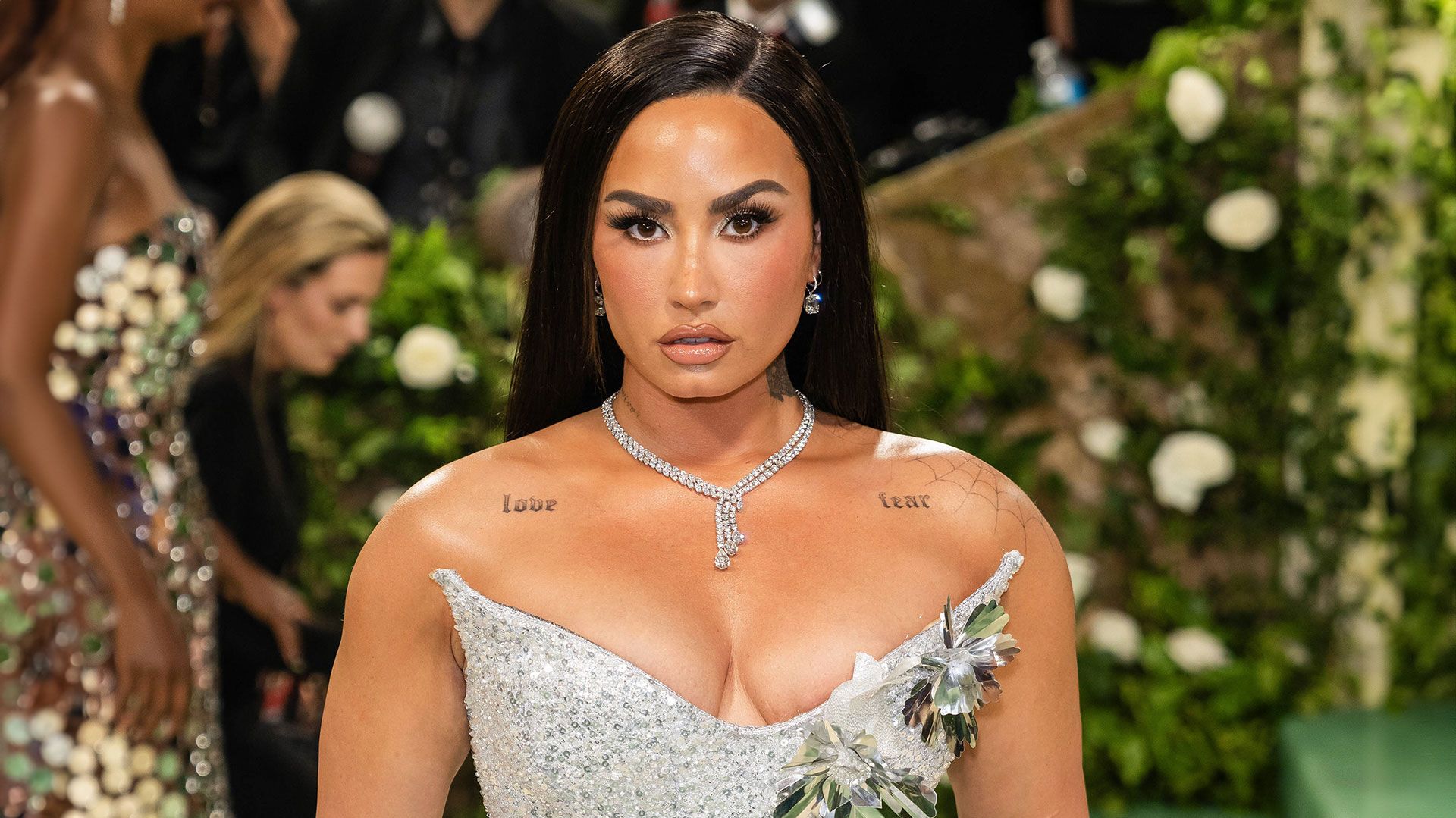 Demi Lovato posing on the red carpet in a sparkling silver gown, looking glamorous and radiant.