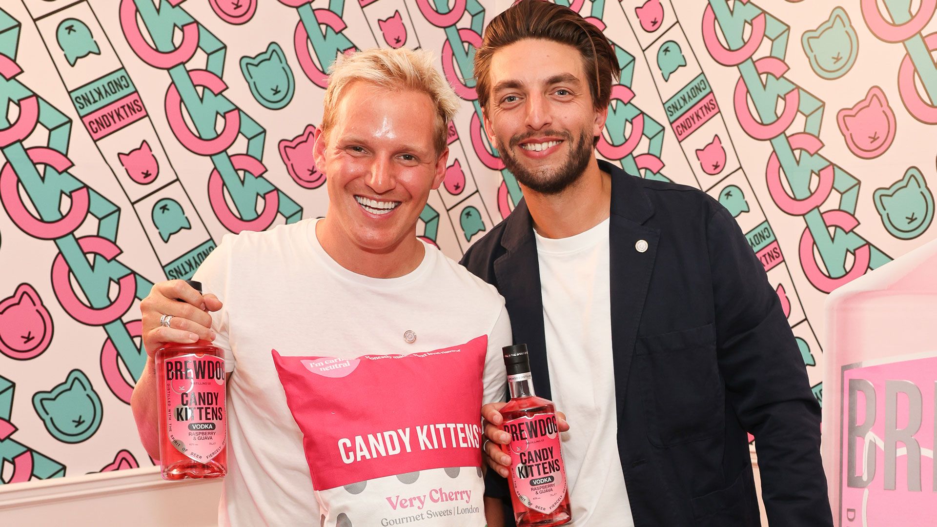 Jamie Laing and his business partner posing with a display of Candy Kittens products, smiling at the camera and showcasing the brand’s colorful vegan sweets lineup.