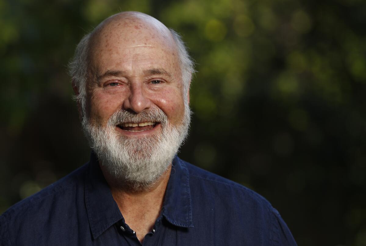 Rob Reiner smiling during an interview outdoors with trees in the background