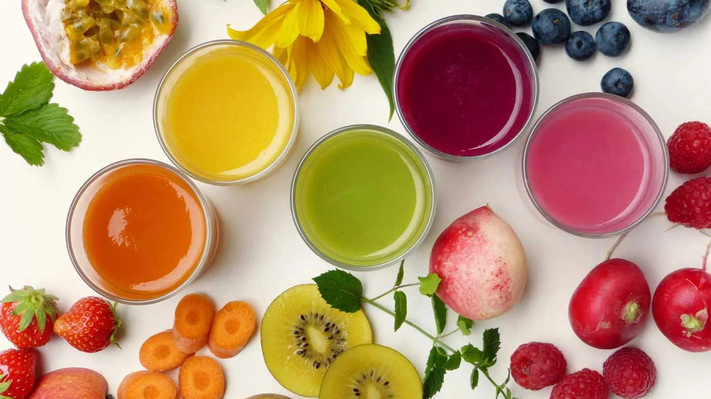 A vibrant display of colorful fruits and matching smoothies made from them, arranged on a table.