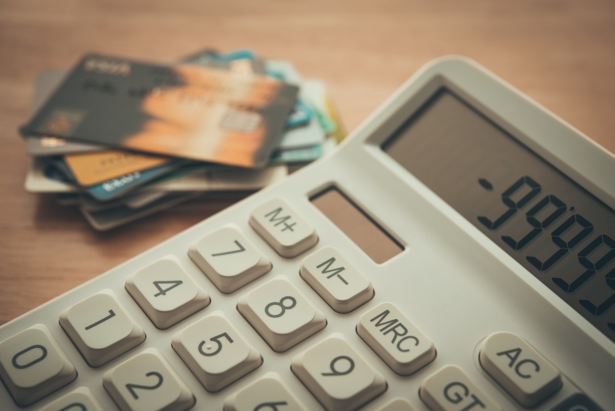 white calculator shows minus delinquent and many credit cards on wooden table background.