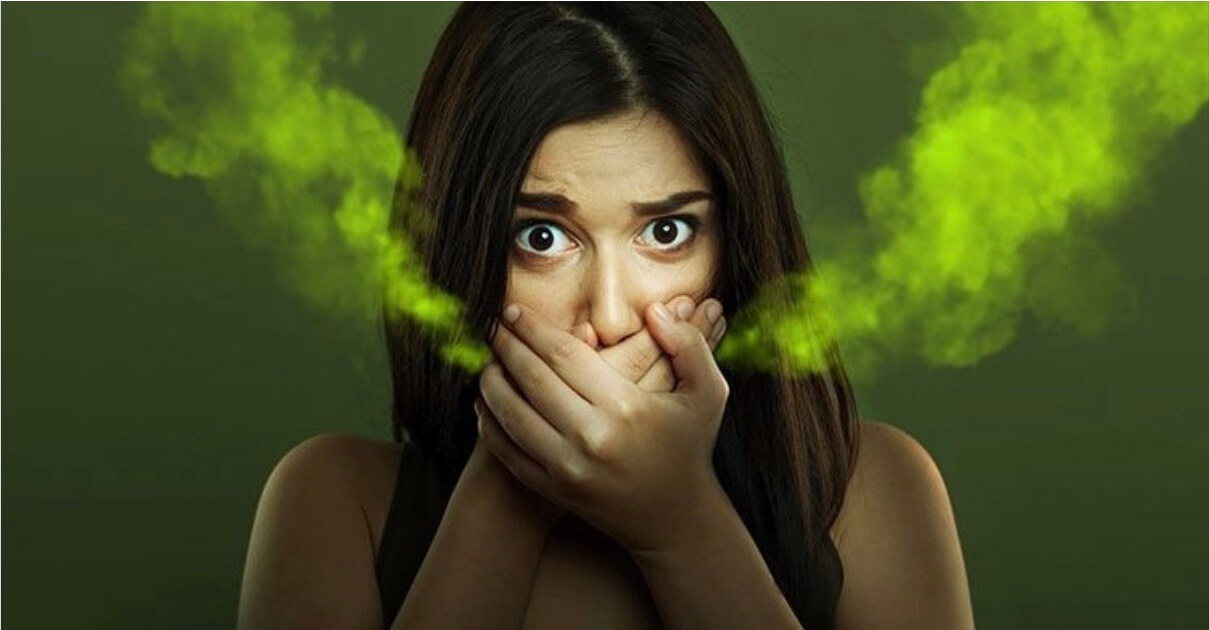 Woman covering her mouth with green mist emanating, symbolizing bad breath or halitosis.