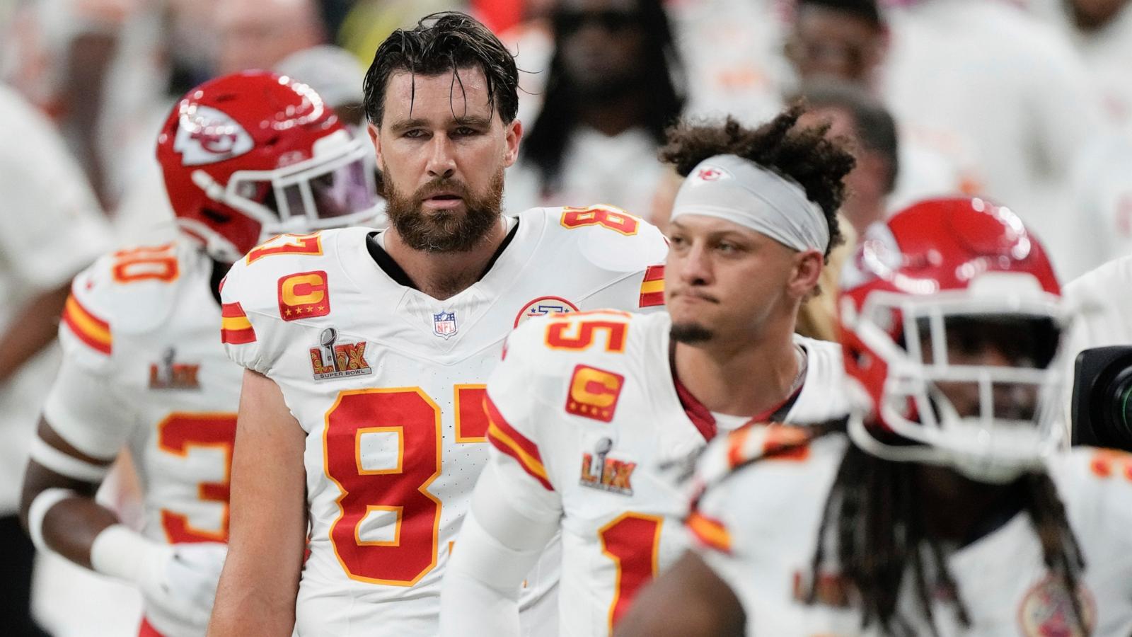Patrick Mahomes and Travis Kelce standing side by side on the field after a game, helmets off, looking focused as they prepare to leave the field.