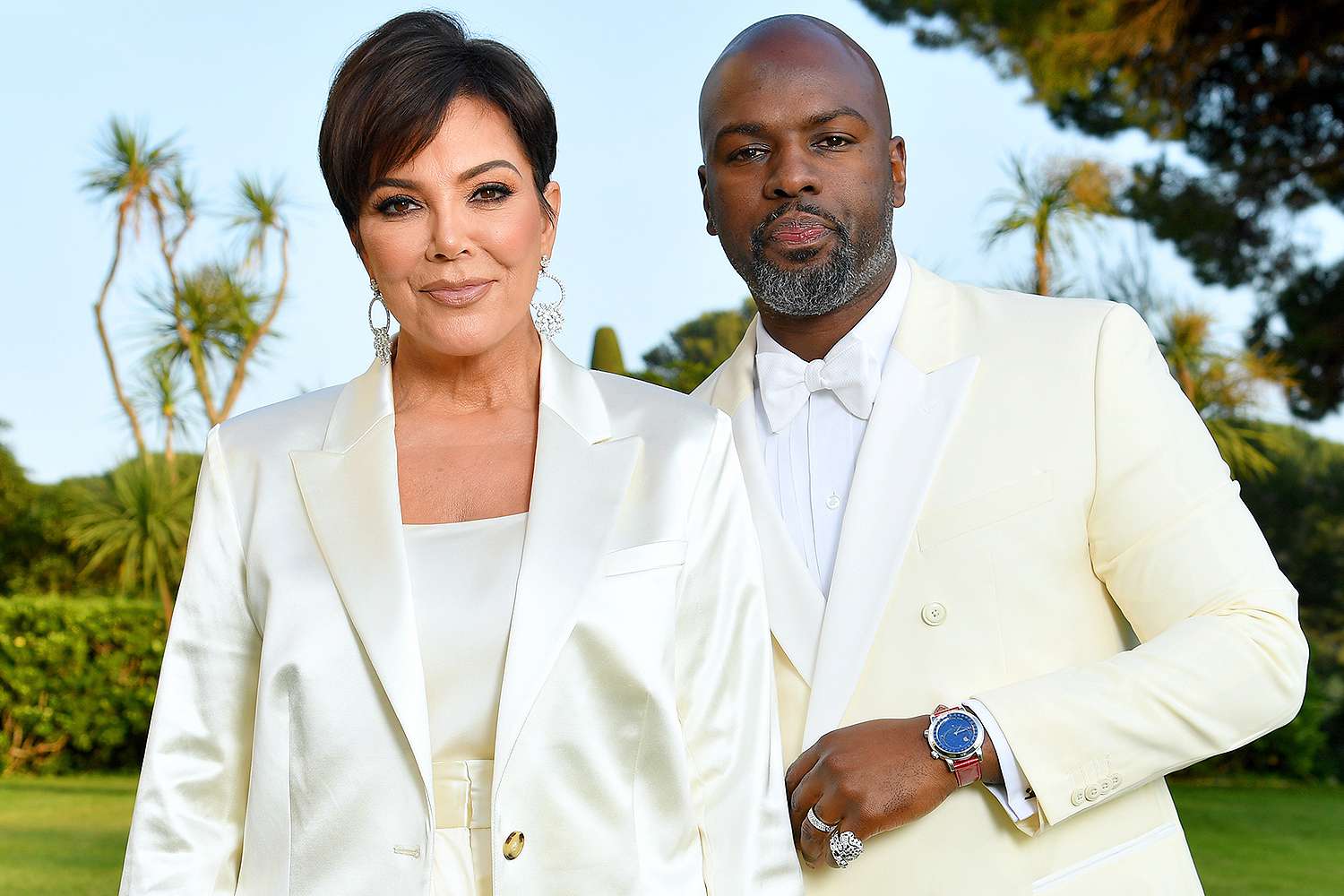 Kris Jenner and Corey Gamble posing together in matching white suits, looking stylish and coordinated.