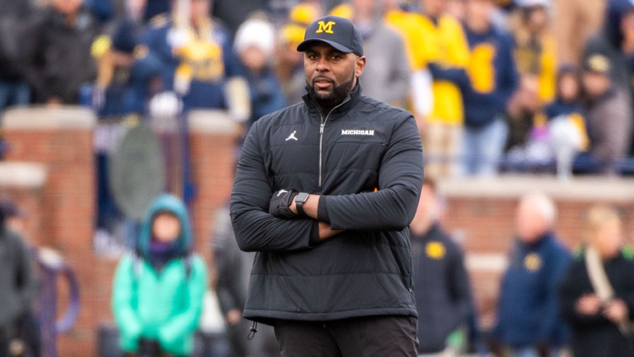 Sherrone Moore standing on the sidelines in Michigan gear, headset on, focused as he coaches during a game, reflecting his rise from offensive line mentor to head coach.