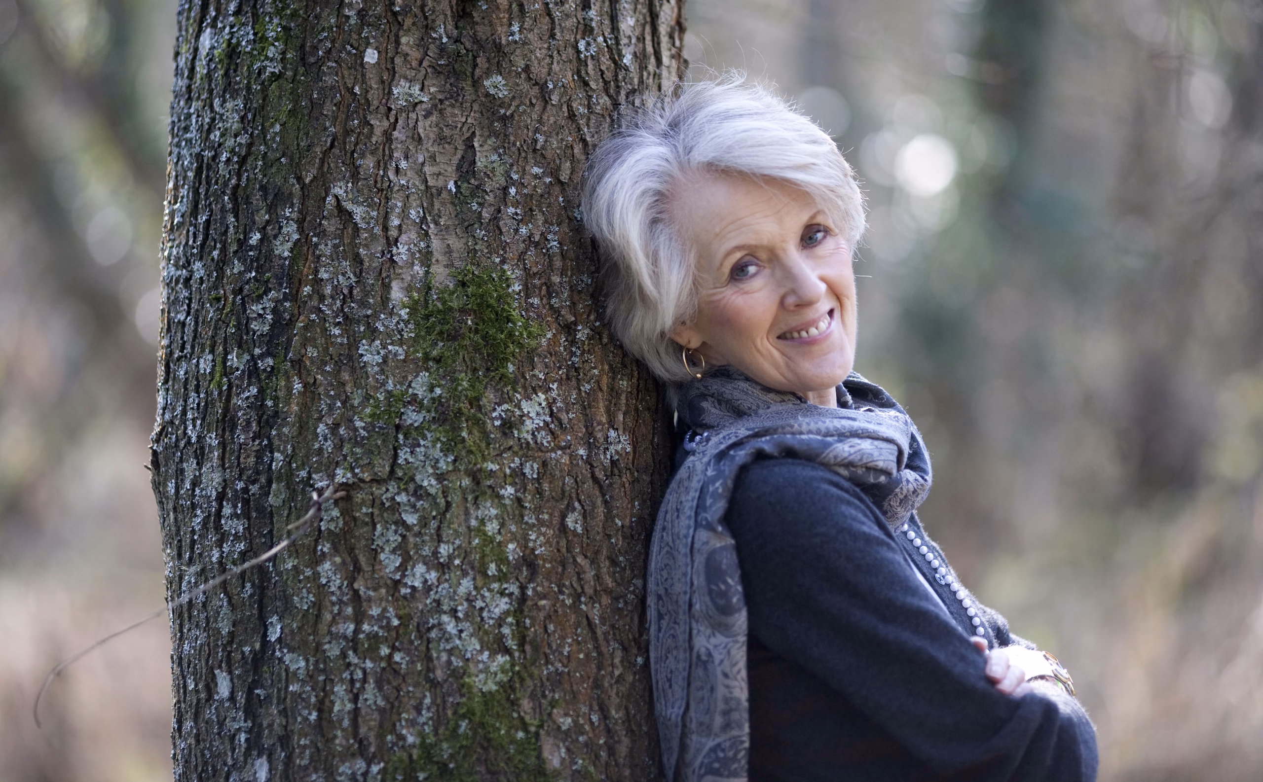 Joanna Trollope smiling and posing against a tree outdoors, dressed casually and looking relaxed.