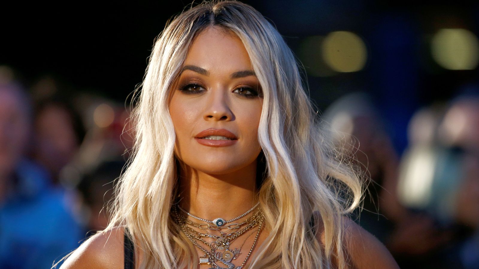 Rita Ora smiling directly at the camera on the Fashion Awards red carpet, wearing a plunging silver gown and slicked-back hair.