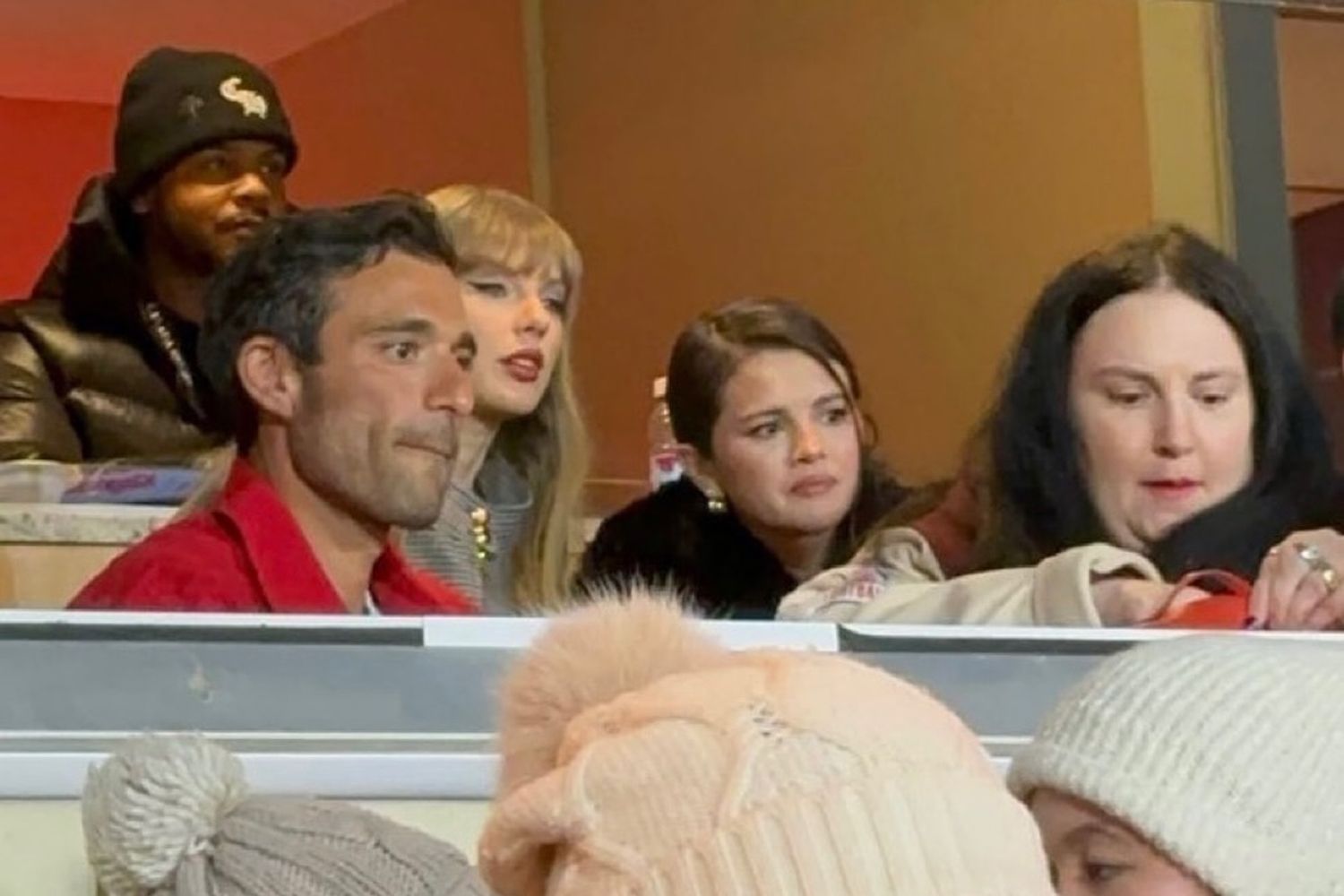 Taylor Swift and Selena Gomez watching the Chiefs game intently from the stands, focused on every play at Arrowhead Stadium.