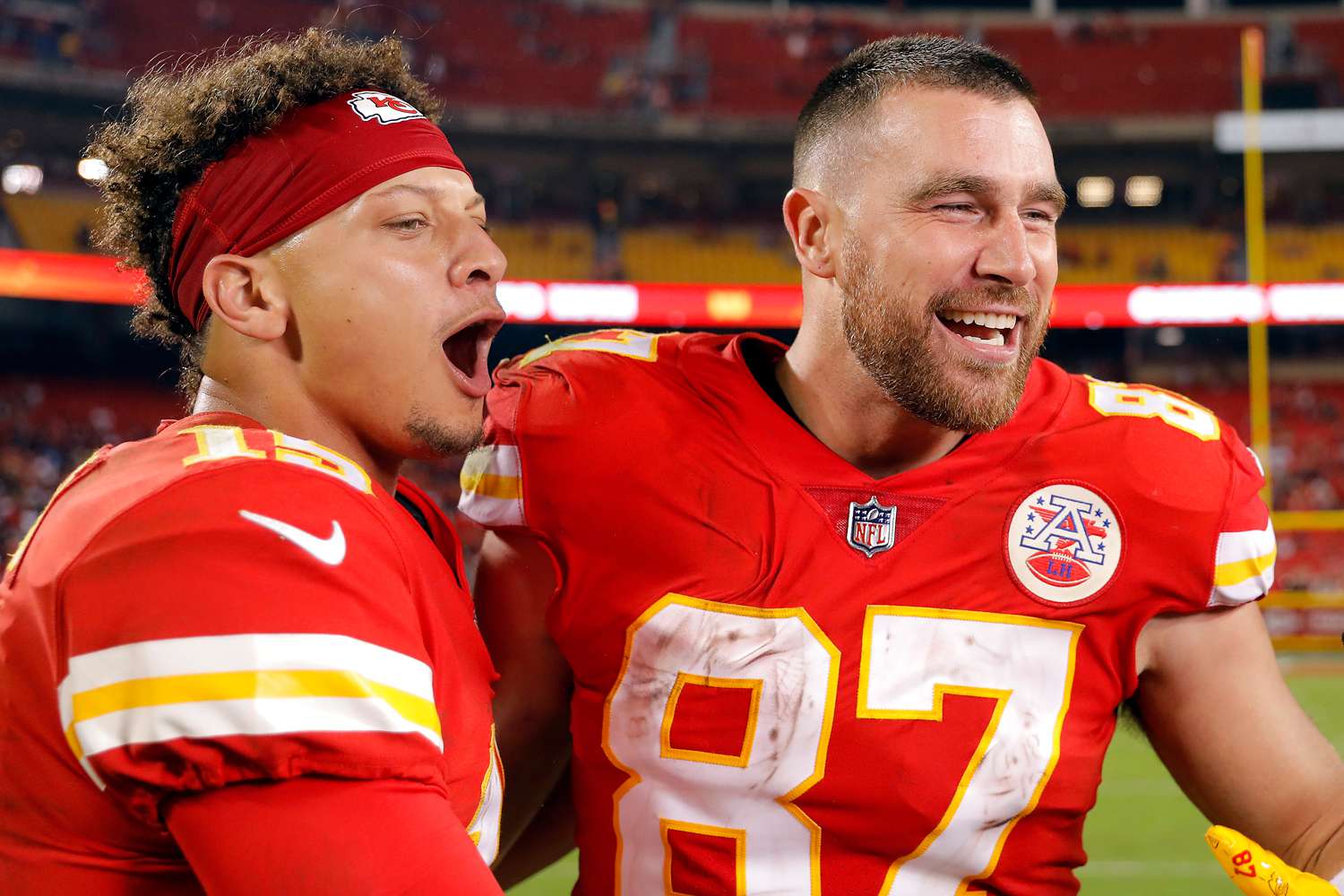 Patrick Mahomes and Travis Kelce celebrating together on the field, smiling and embracing after a big play, with the stadium lights glowing behind them.