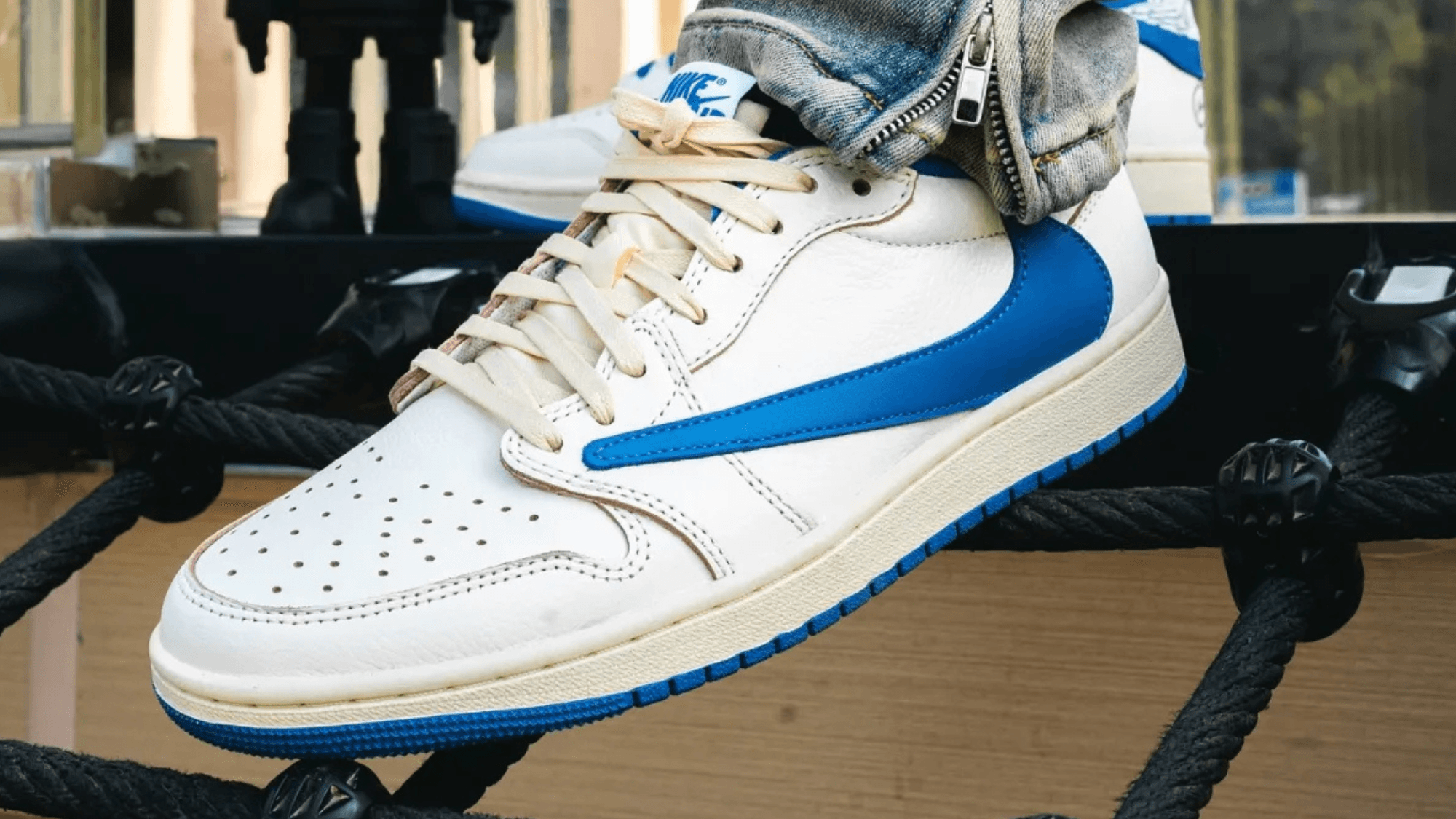 Close-up of a white and blue Nike Air Jordan sneaker with laces and perforated toe, displayed on a black rope platform
