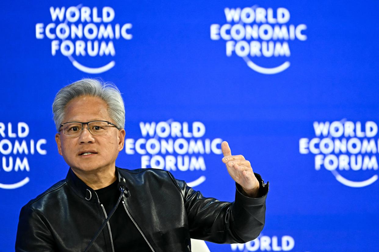 Nvidia CEO speaking on stage at the World Economic Forum, gesturing during a panel discussion on AI and jobs.