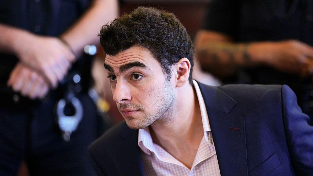 Luigi Mangione wearing a suit in court, standing during proceedings, facing federal charges.