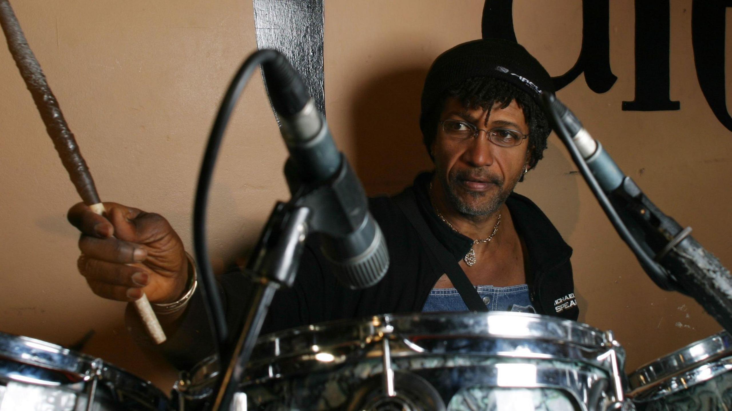 Sly Dunbar seated at his drum kit in a recording studio, focused on creating rhythms that shaped reggae and global music.