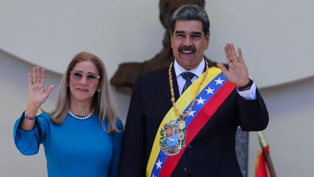 Cilia Flores and Nicolás Maduro wave to a cheering crowd in Venezuela, symbolizing their political influence and presence at a public rally.