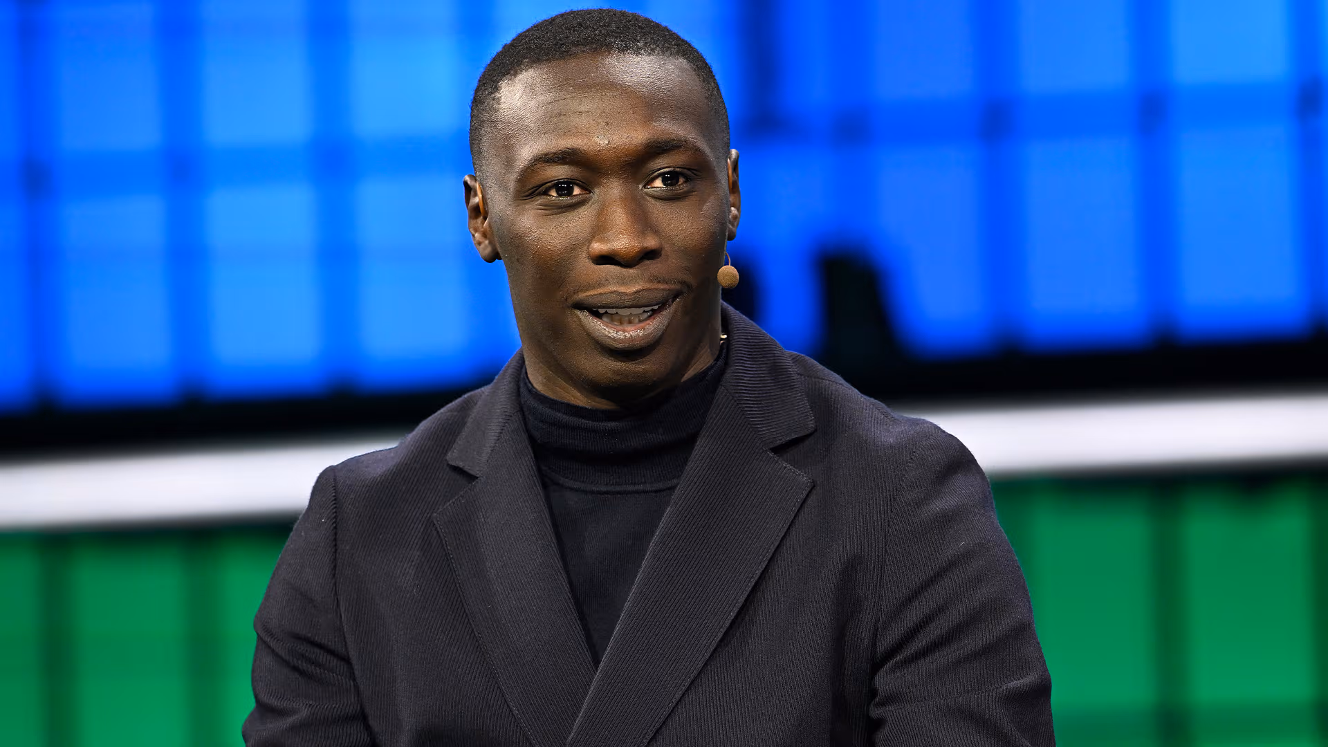 Khaby Lame speaking on stage during a summit, addressing an audience about his career and creative process