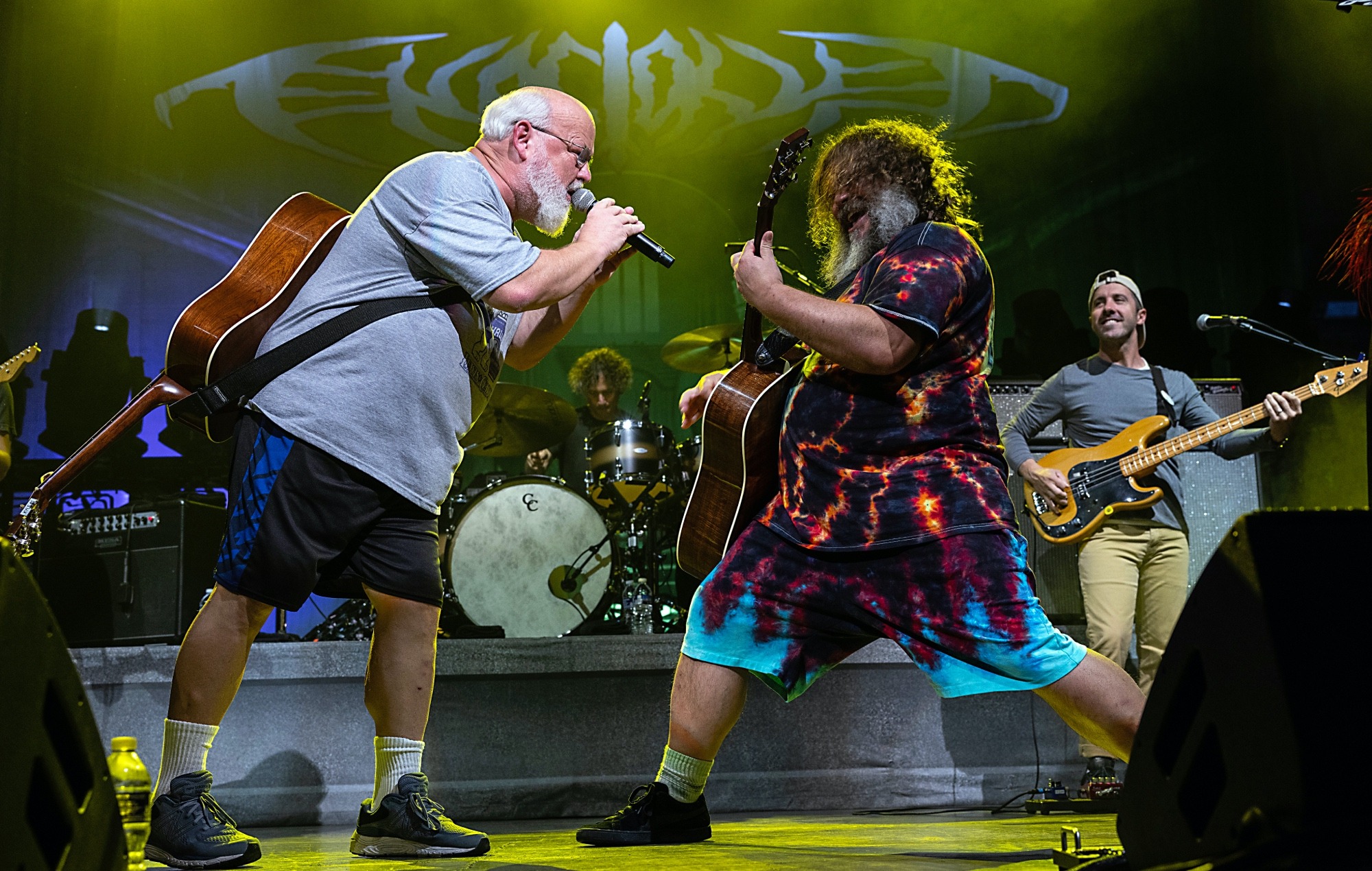 Tenacious D performing on stage during the controversial concert where Kyle Gass made a joke about Donald Trump’s assassination attempt, with Jack Black reacting behind him and the crowd in the background.