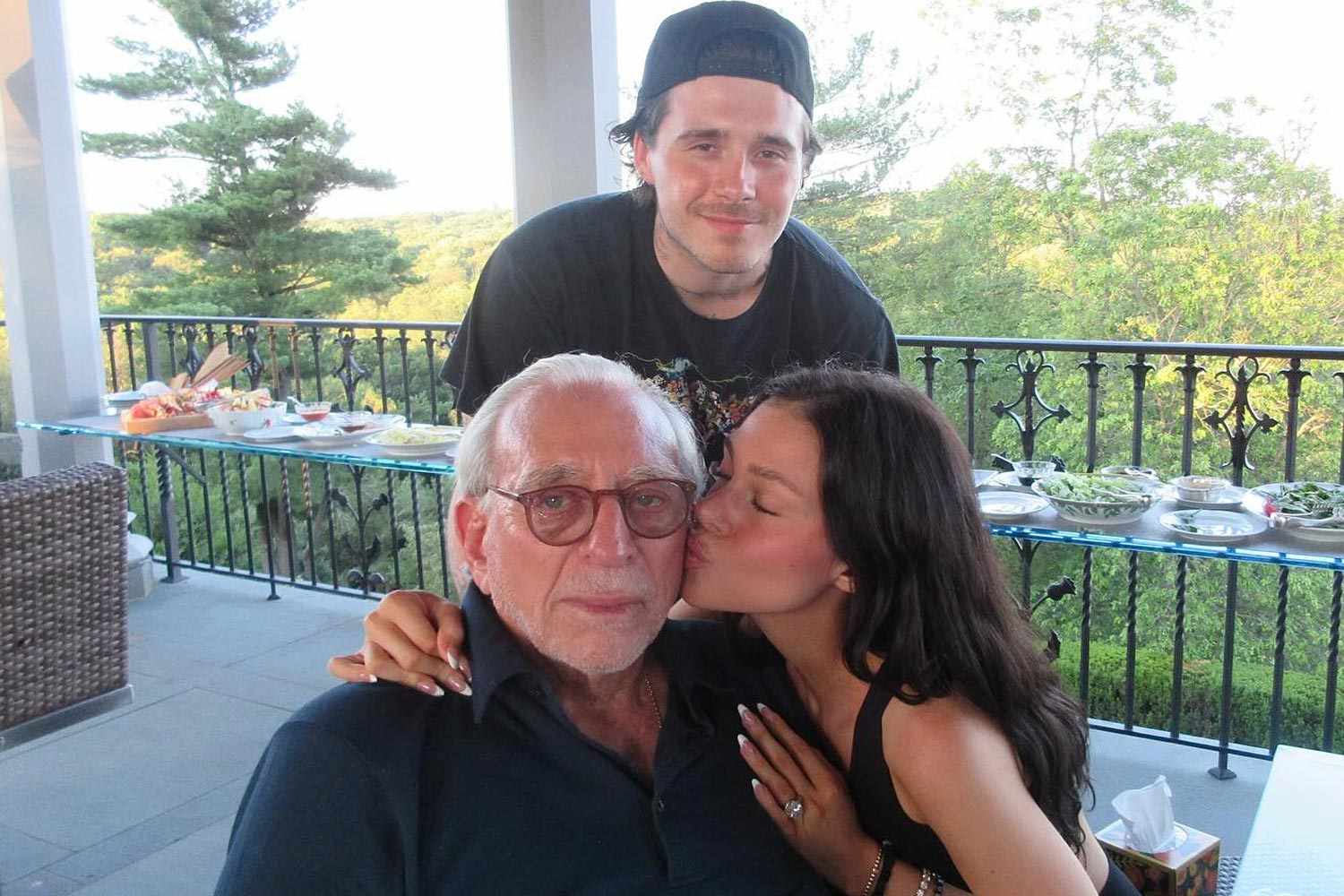 Brooklyn Beckham stands behind wife Nicola Peltz as she kisses her father, Nelson Peltz, on the cheek, capturing a candid family moment amid billionaire and celebrity circles.