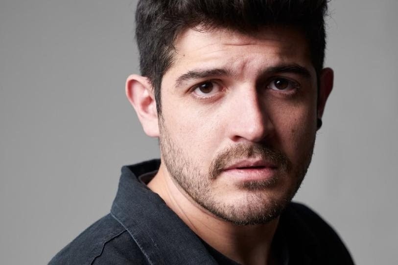 Alexis Ortega looking directly at the camera during a professional photoshoot, wearing a casual blazer and neutral background.