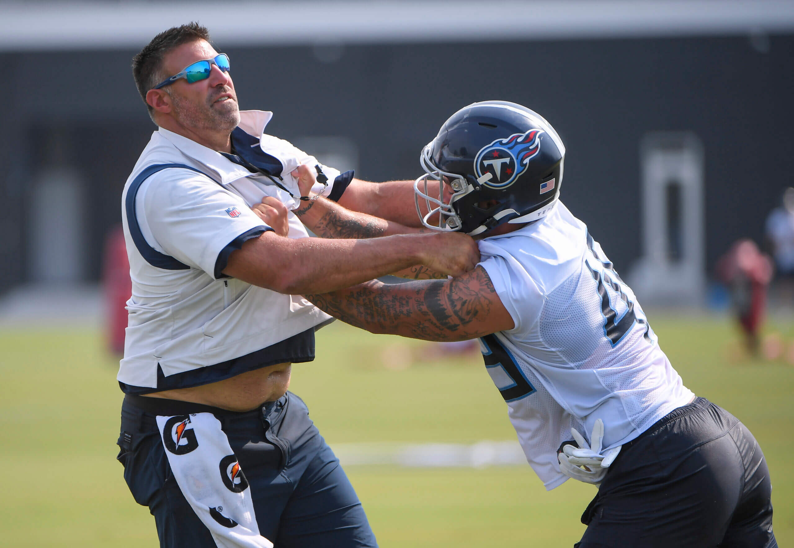 Mike Vrabel demonstrating a tackling technique with a player during Patriots training camp, emphasizing hands-on coaching.