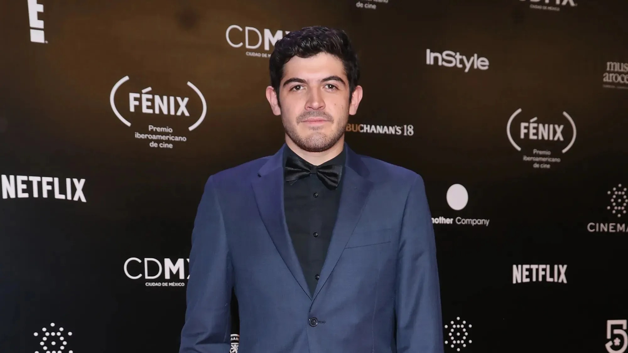 Alexis Ortega posing on the red carpet in a suit, smiling at photographers at a film premiere.