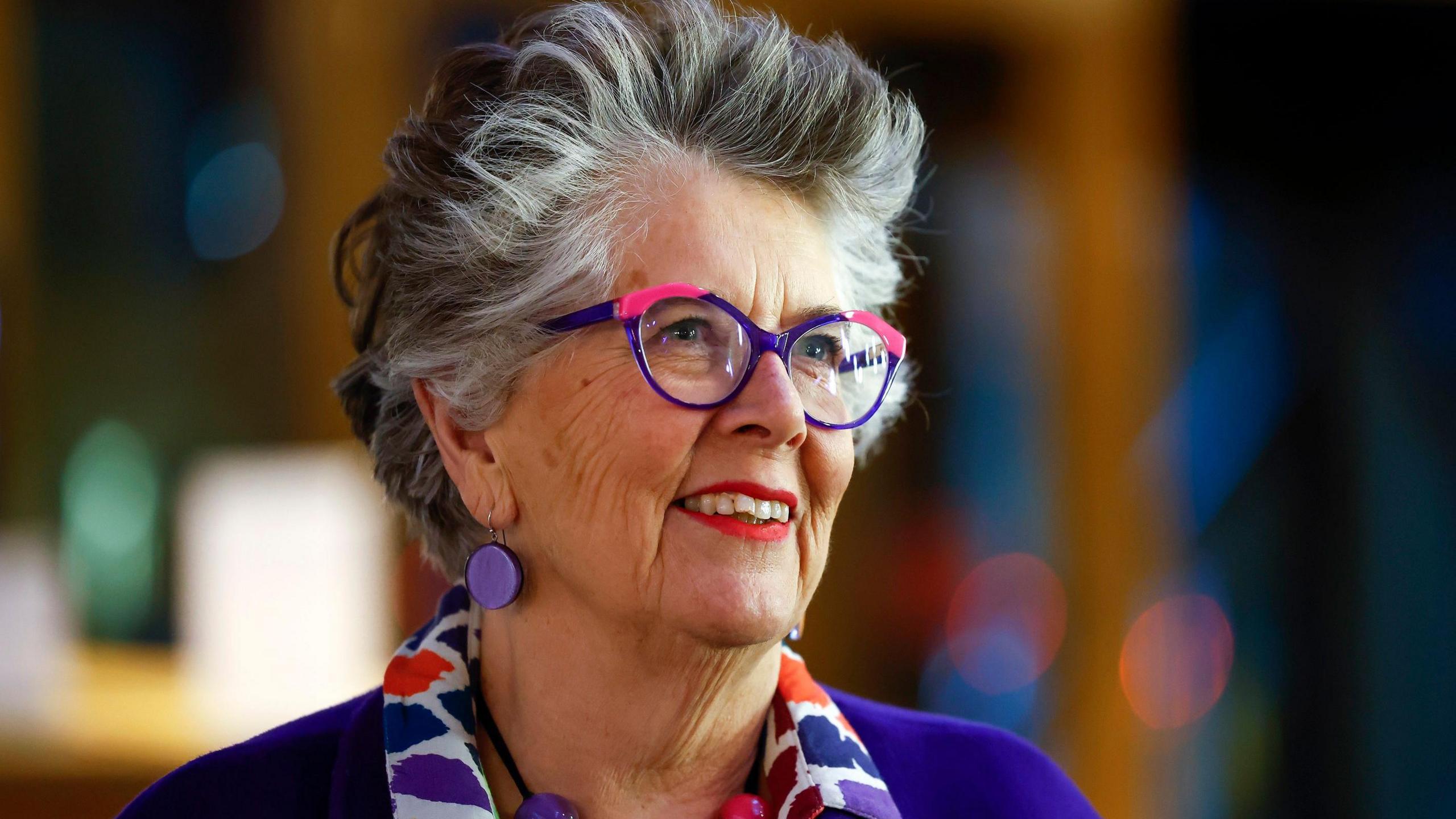 Prue Leith smiling during a televised interview, wearing a colorful blazer and speaking with warmth and charm.