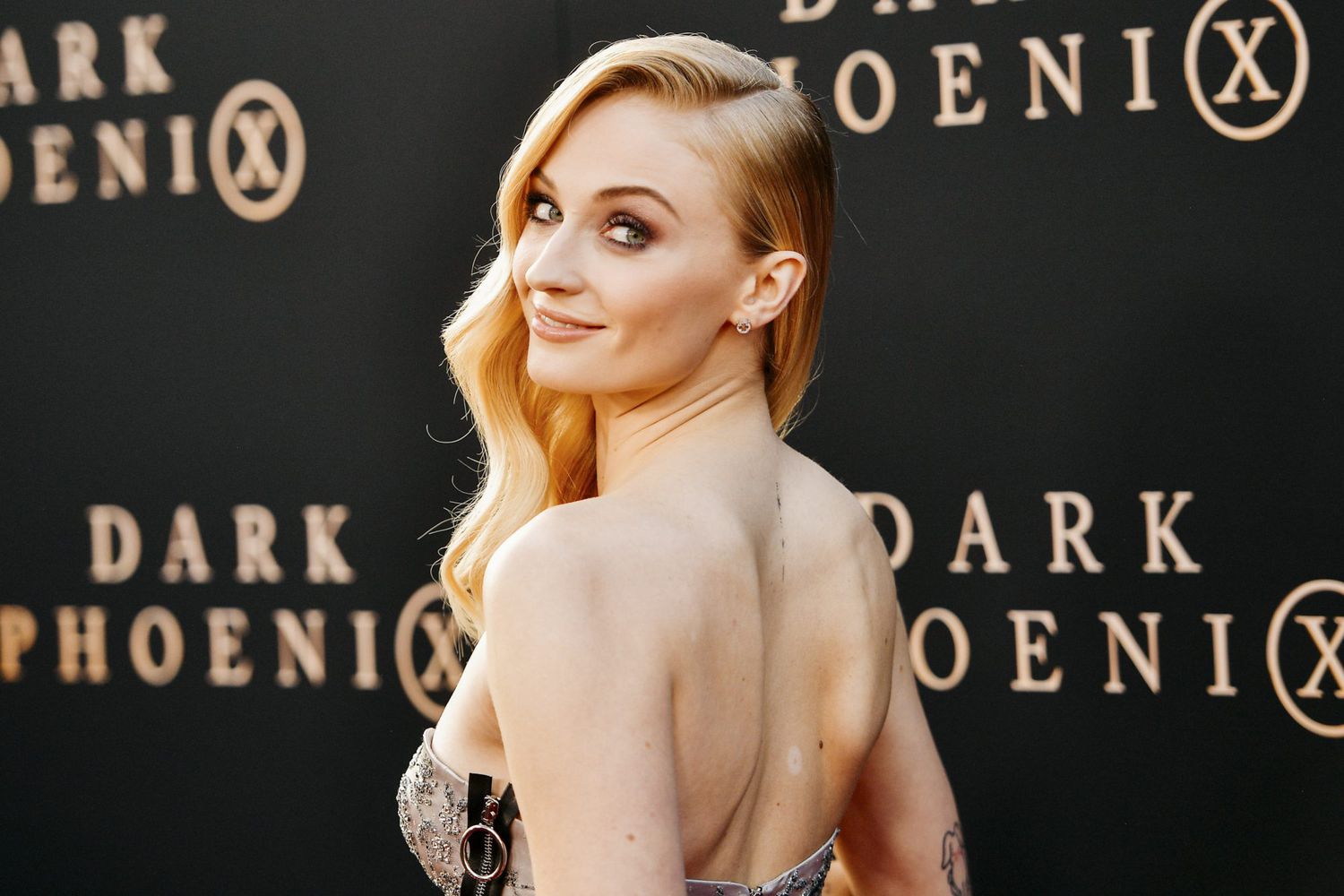 Sophie Turner smiling on the red carpet, wearing an elegant gown, exuding Hollywood glamour and confidence.