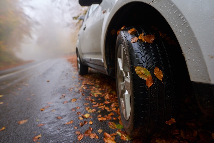closeup of a car with leaves stuck on wheels on a wet road in the autumn