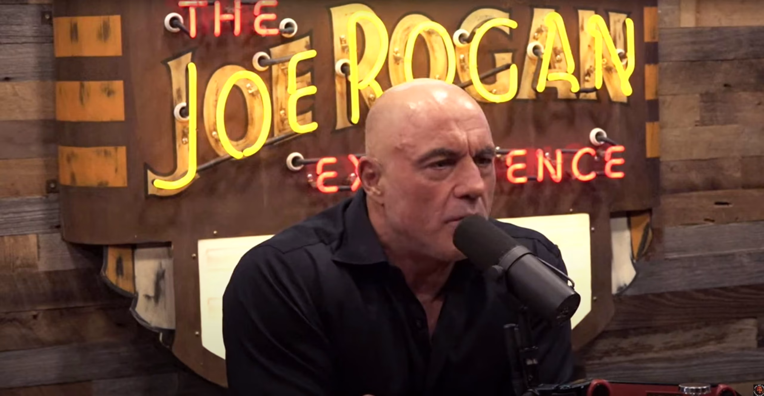 Joe Rogan recording an episode of The Joe Rogan Experience in his Austin podcast studio, engaging with a guest and discussing trending topics.