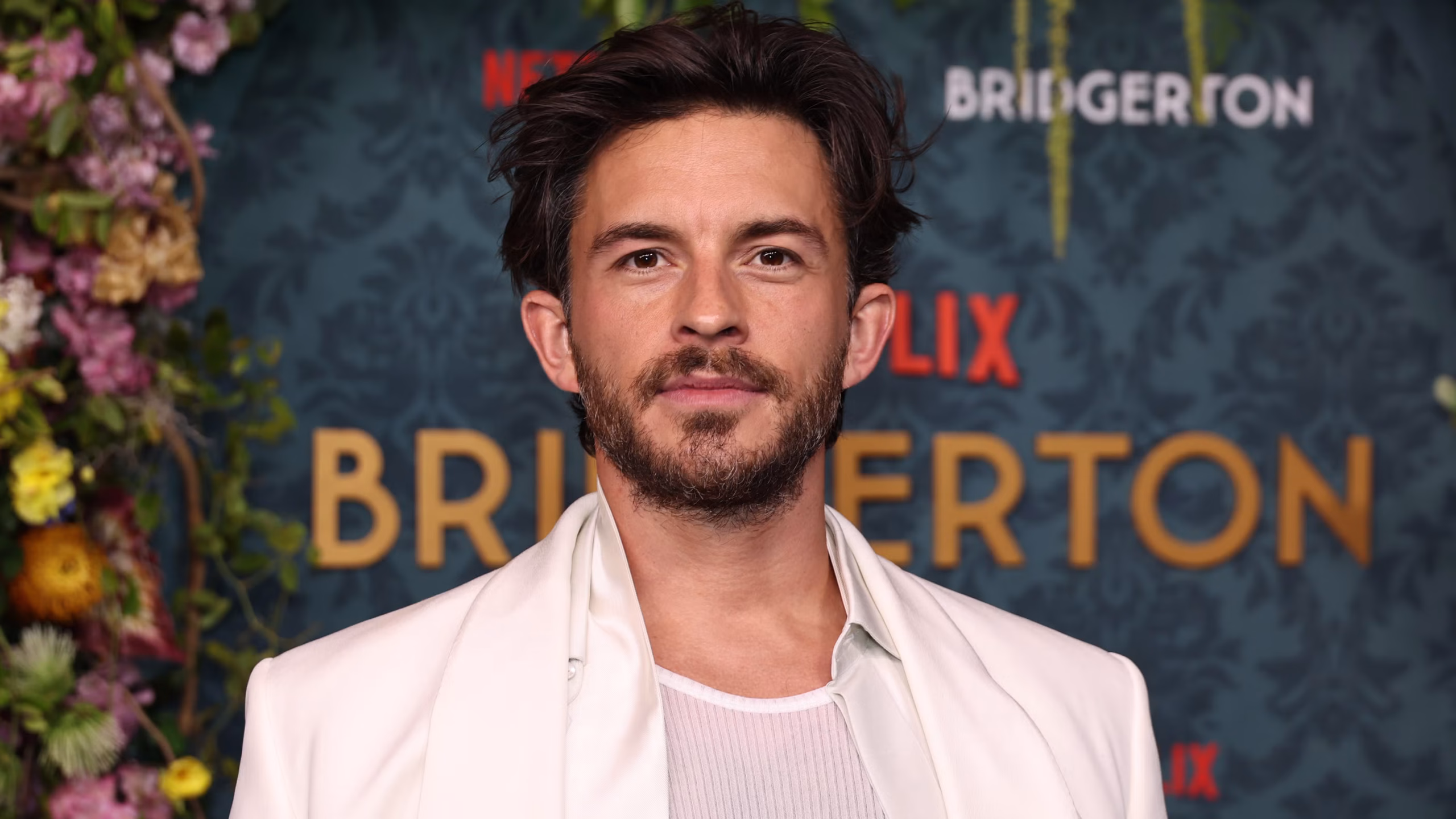 Jonathan Bailey on the Bridgerton red carpet, wearing a sharp suit and smiling for photographers.
