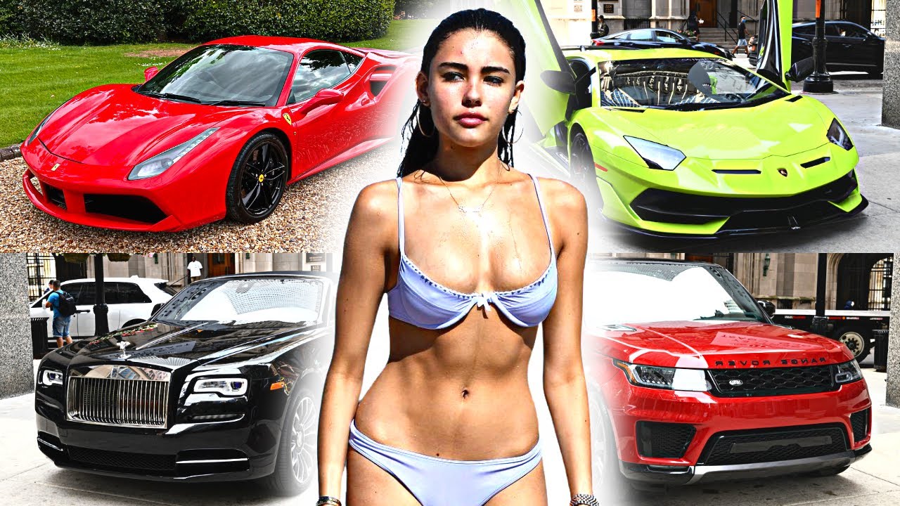 Madison Beer standing amidst her luxury car collection, including a Lamborghini, Ferrari, Mercedes-AMG, and Range Rover, showcasing her taste for high-performance vehicles.