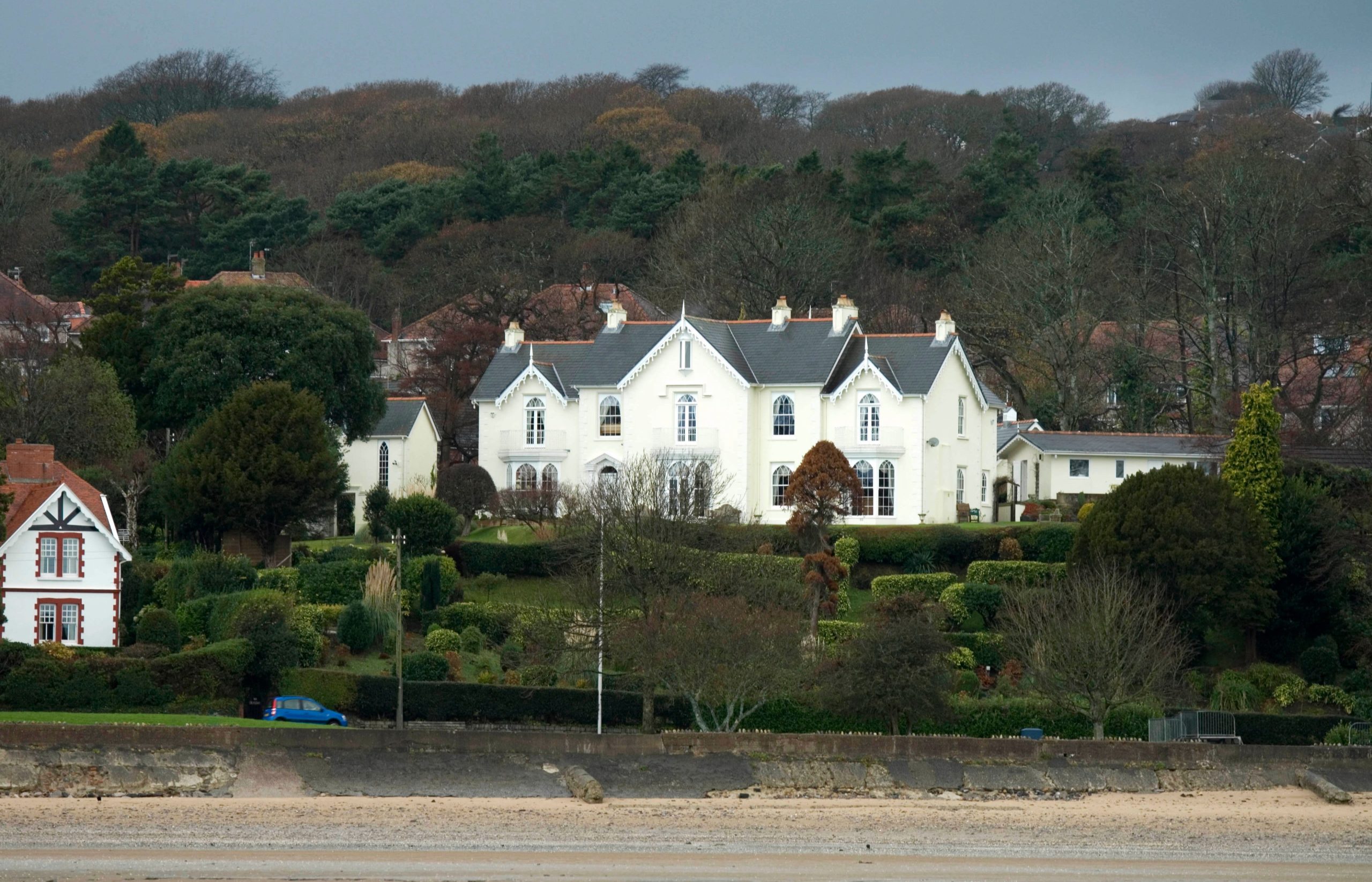 A modern, high-end seaside villa with a bright white exterior and large glass panels. The home features a luxury swimming pool in the foreground, reflecting the coastal sunlight, with the Atlantic Ocean visible in the distance.