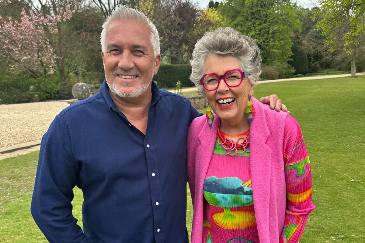 Prue Leith and Paul Hollywood smiling together for a photo, dressed smartly and exuding camaraderie on set.