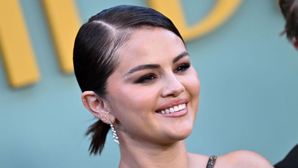 Selena Gomez attends a public event with hair slicked back, wearing diamond drop earrings and natural makeup.