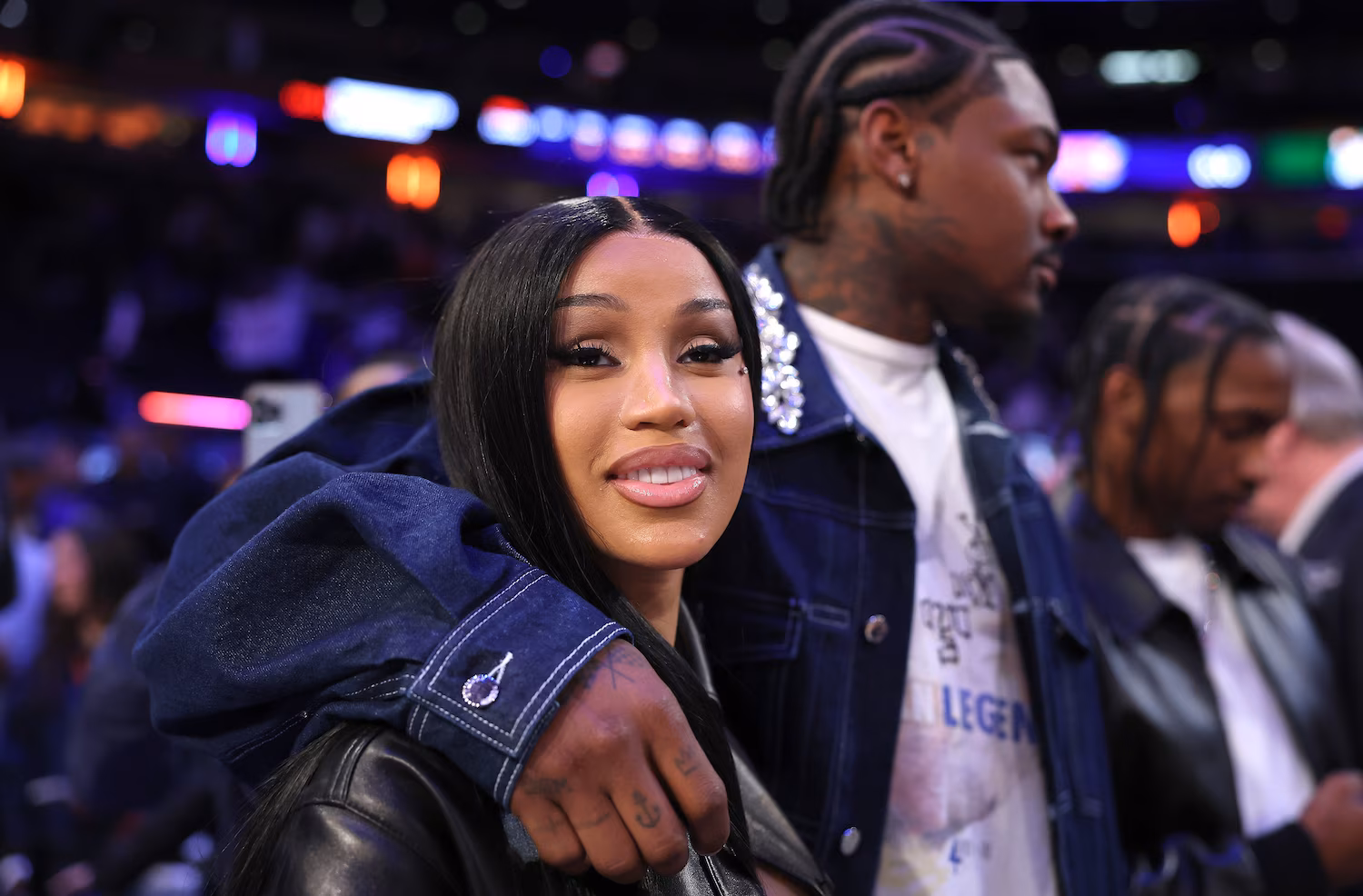 Cardi B and Stefon Diggs hugging courtside at an NBA game, smiling and showing affection in front of fans.