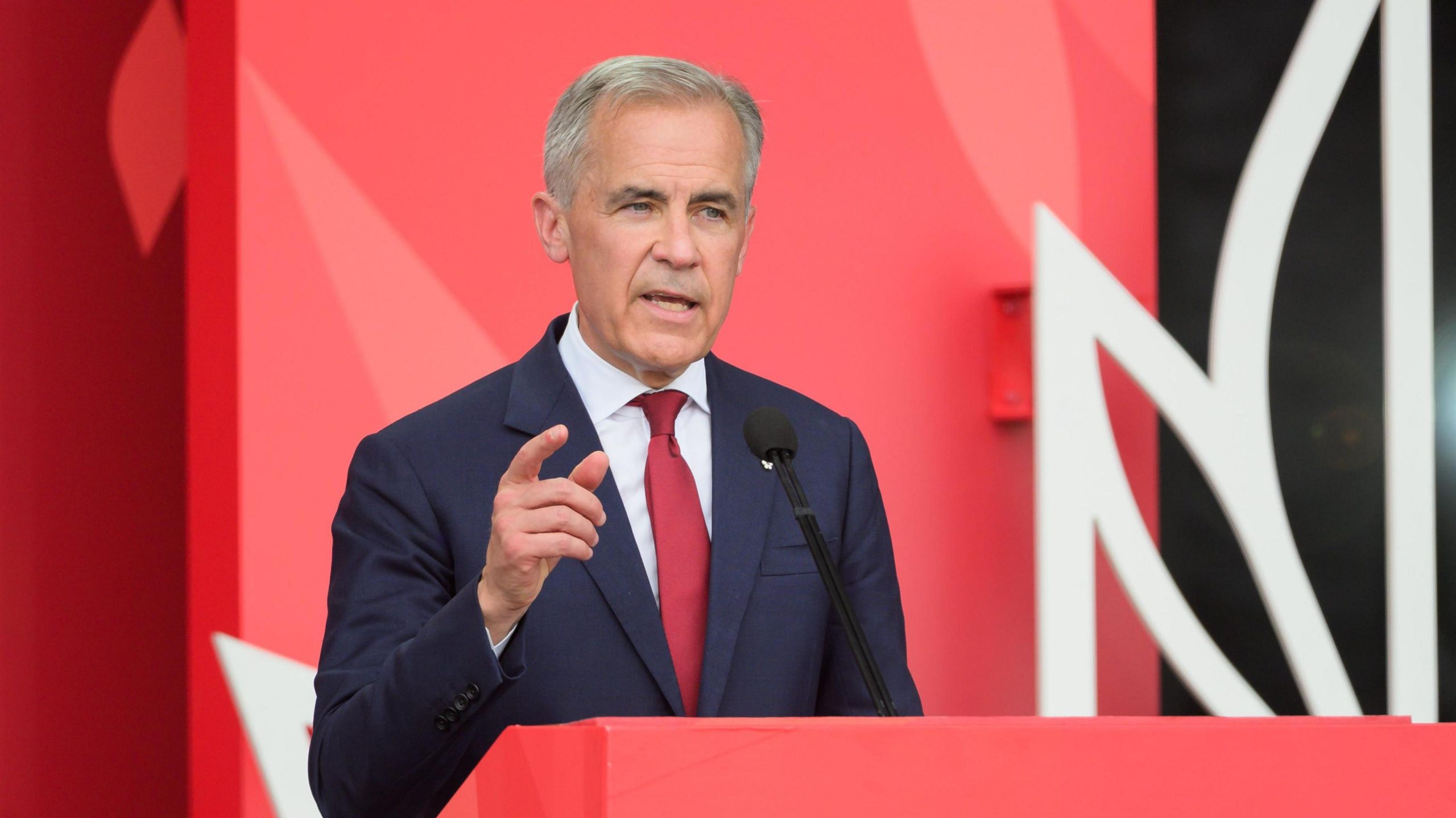 Canadian Prime Minister Mark Carney speaking at a podium about US tariffs and the impact on Canada’s auto industry, addressing trade tensions with President Trump.