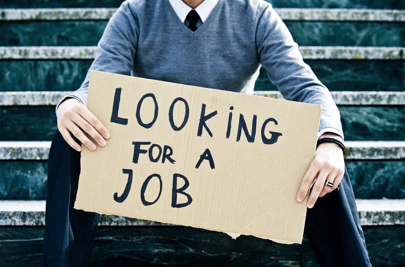 A professionally dressed man holds a sign reading "Looking for Work," highlighting the impact of widespread job cuts in the U.S.