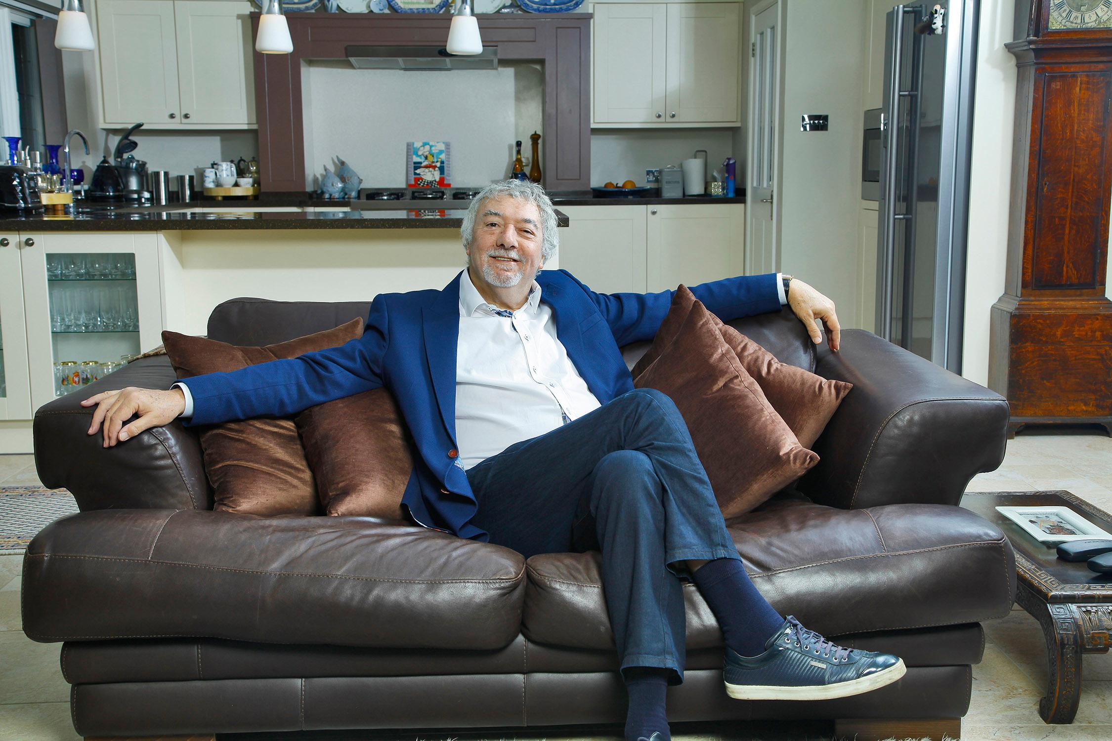 John Virgo seated on a sofa in his living room during a television interview, speaking candidly.