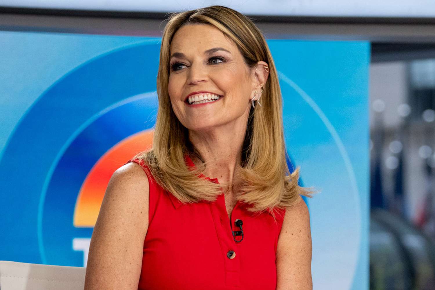 Savannah Guthrie hosting the Today show from the studio, seated at the anchor desk with bright lights and screens in the background.
