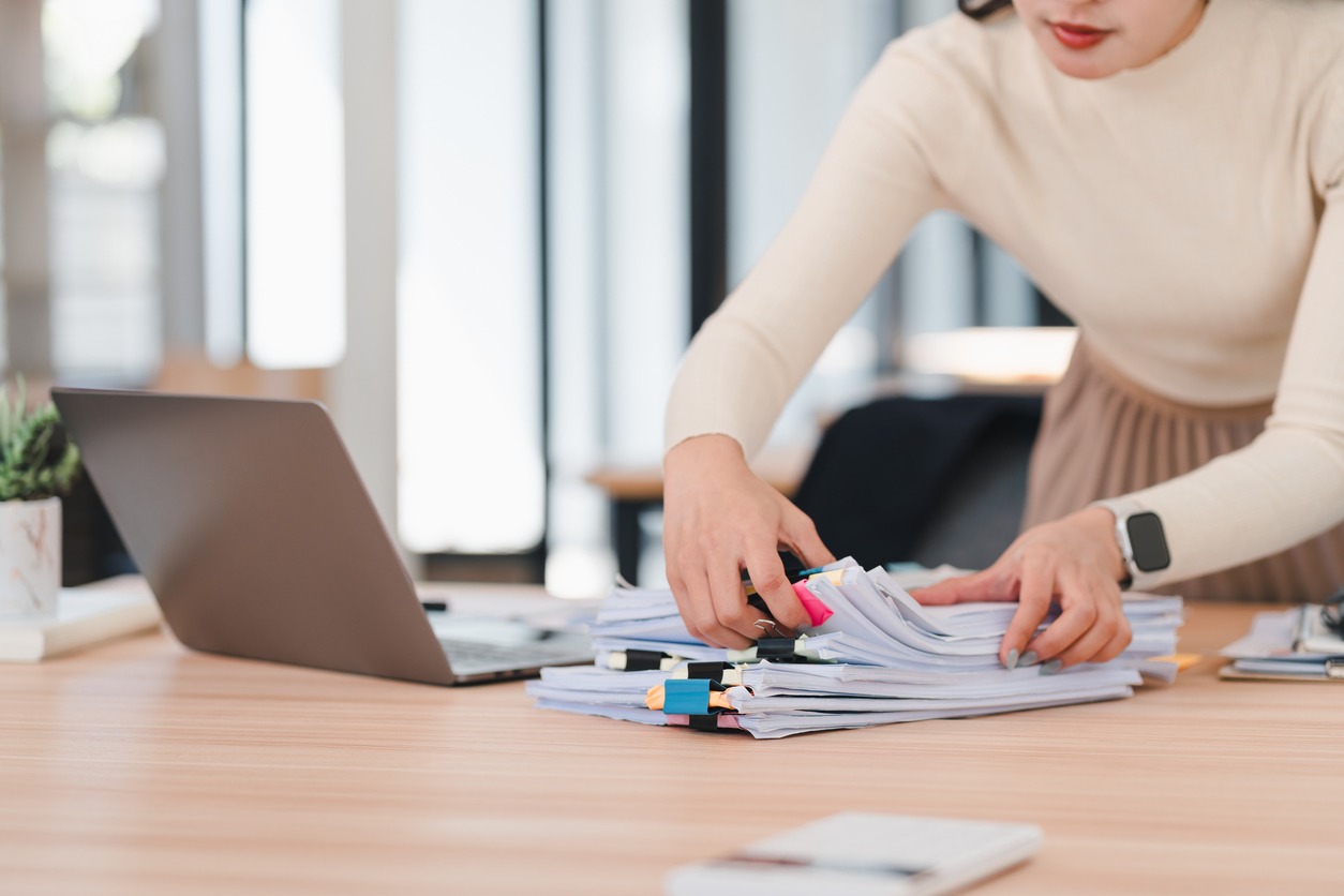 organized asian woman sorting paperwork at desk with laptop, showcasing productivity and focus.