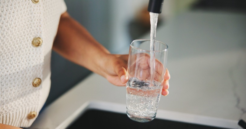 glass, water and tap with hands of woman in kitchen for detox drinks, mineral hydration and health in home. electrolytes, wellness and aqua with person for faucet, liquid or beverage in apartment